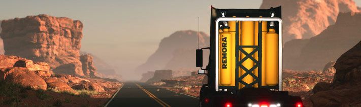 Truck cab driving by mountains without a trailer attached. Four tall tanks are attached to the back of the cab. 